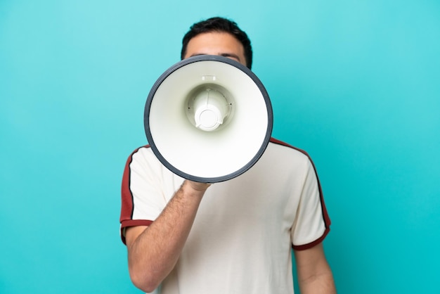 Young Brazilian man isolated on blue background shouting through a megaphone to announce something