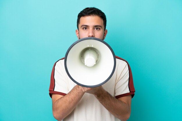 Young Brazilian man isolated on blue background shouting through a megaphone to announce something