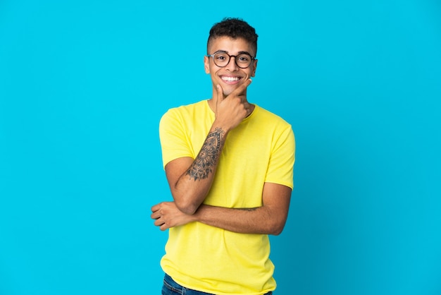 Giovane uomo brasiliano isolato sulla parete blu felice e sorridente