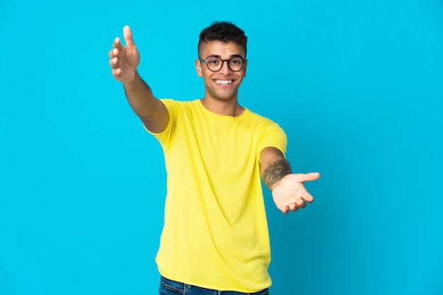 Young Brazilian man isolated on blue wall presenting and inviting to come with hand