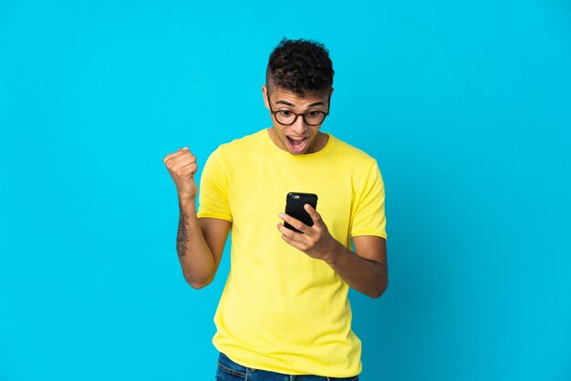 Young Brazilian man isolated on blue wall surprised and sending a message