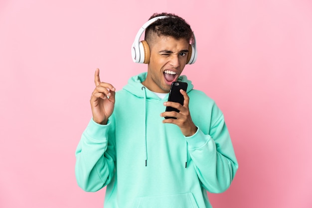 Young Brazilian man over isolated listening music with a mobile and singing