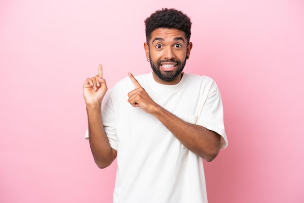 Young Brazilian man isolated on pink background frightened and pointing to the side