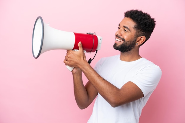 Young Brazilian man isolated on pink background shouting through a megaphone to announce something