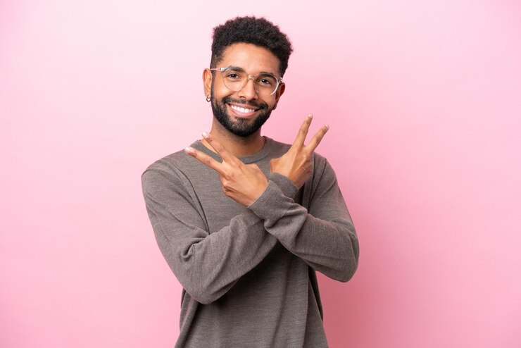 Photo 笑顔と勝利のサインを示すピンクの背景に孤立した若いブラジル人男性