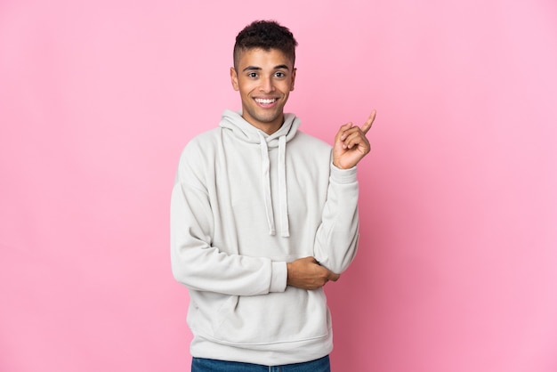 Young Brazilian man isolated on pink space happy and pointing up