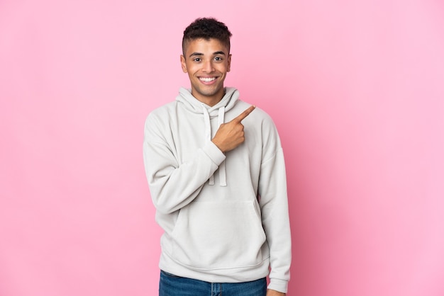 Young Brazilian man isolated on pink wall pointing to the side to present a product