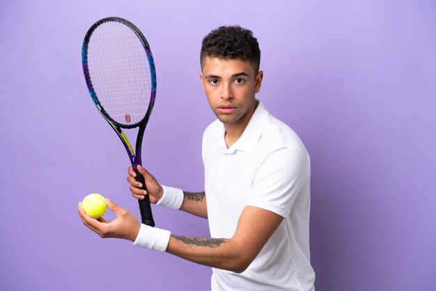 Young brazilian man isolated on purple background playing tennis