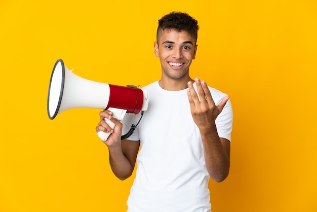 メガホンを持って、手で来るように誘う孤立したスペース上の若いブラジル人男性