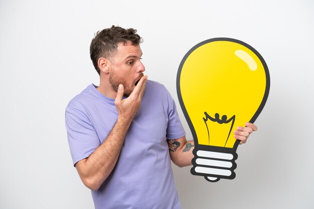 Young Brazilian man isolated on white background holding a bulb icon with surprised expression