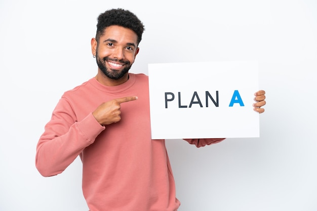 Young Brazilian man isolated on white background holding a placard with the message PLAN A and pointing it
