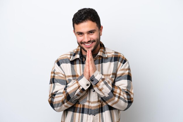 Young Brazilian man isolated on white background keeps palm together Person asks for something