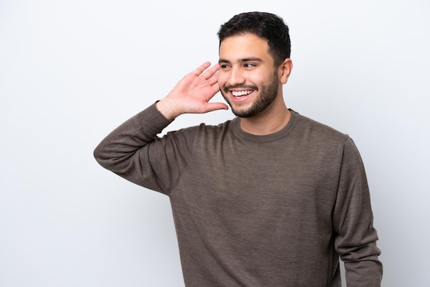 Young Brazilian man isolated on white background listening to something by putting hand on the ear