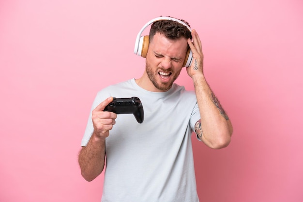 Young Brazilian man playing with video game controller isolated on pink background frustrated and covering ears