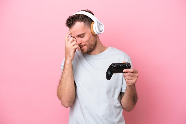 Young Brazilian man playing with video game controller isolated on pink background laughing