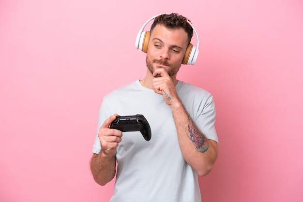 Young Brazilian man playing with video game controller isolated on pink background looking to the side and smiling