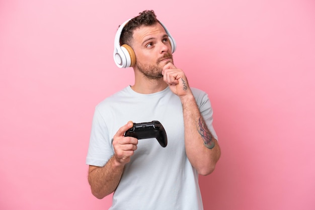 Young Brazilian man playing with video game controller isolated on pink background and looking up