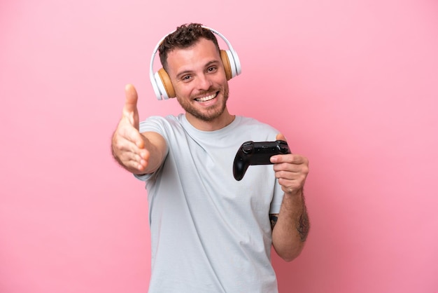 Молодой бразилец, играющий с контроллером видеоигры на розовом фоне, пожимает руку для закрытия хорошей сделки