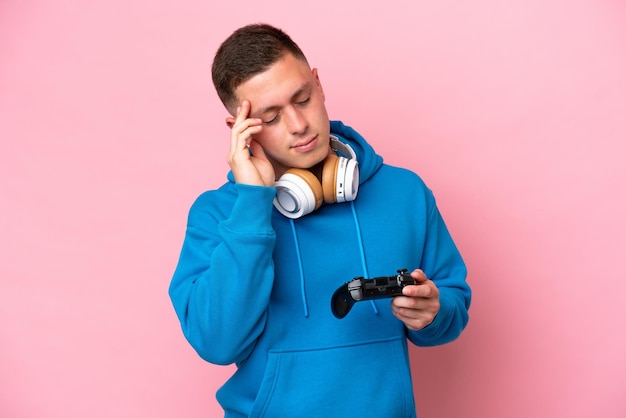 Молодой бразилец играет с контроллером видеоигры на розовом фоне с головной болью