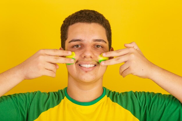 Young brazilian man soccer fan dressed in green and yellow putting paint on his face