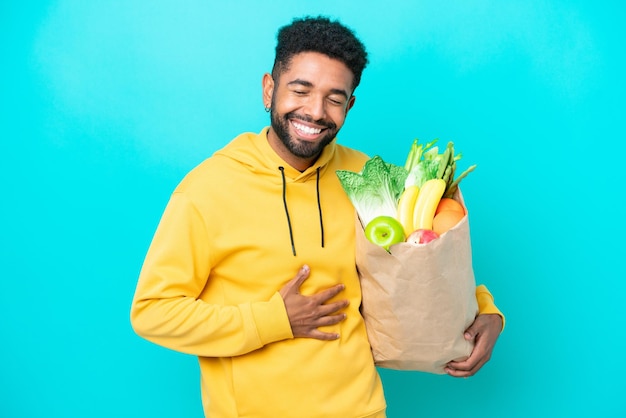 Young Brazilian man taking a bag of takeaway food isolated on blue background smiling a lot