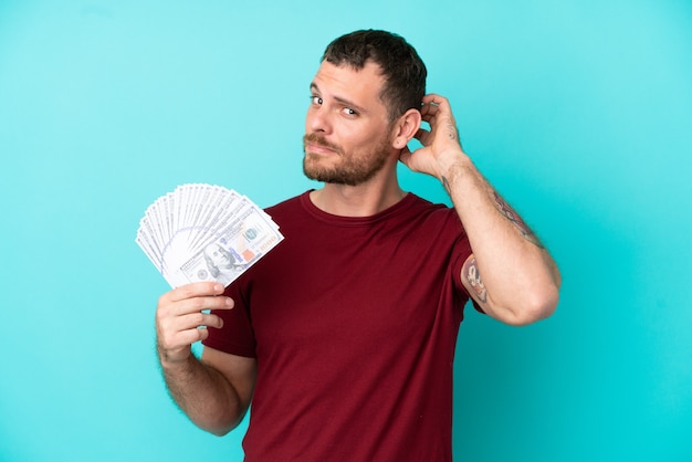 Young Brazilian man taking a lot of money over isolated background having doubts