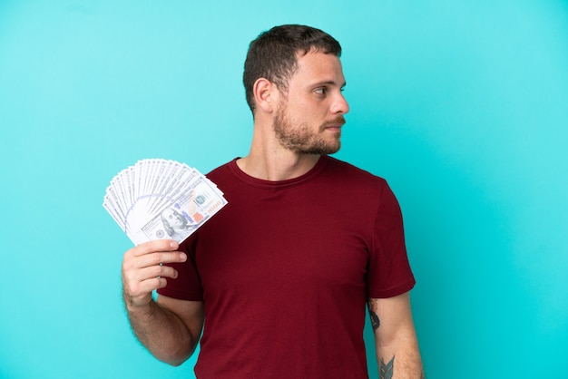 Young Brazilian man taking a lot of money over isolated background looking to the side