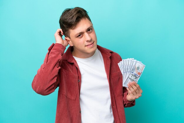 Young brazilian man taking a lot of money isolated on blue background having doubts