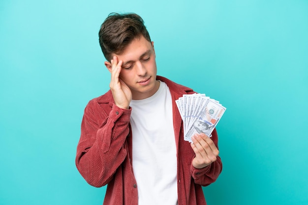 Young brazilian man taking a lot of money isolated on blue background with headache