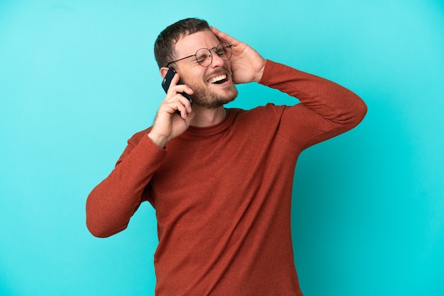 Foto giovane brasiliano che utilizza il telefono cellulare isolato su sfondo blu sorride molto