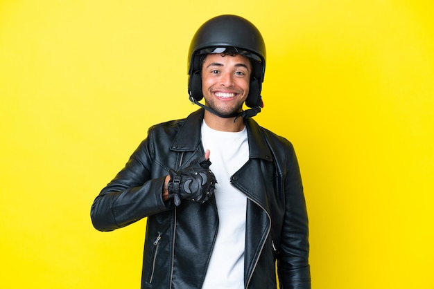 Фото Молодой бразильский мужчина в мотоциклетном шлеме изолирован на желтом фоне, показывая жест рукой вверх