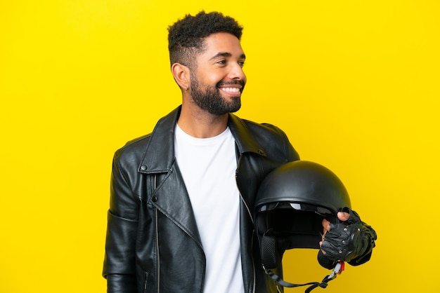 Young Brazilian man with a motorcycle helmet isolated on yellow background looking side