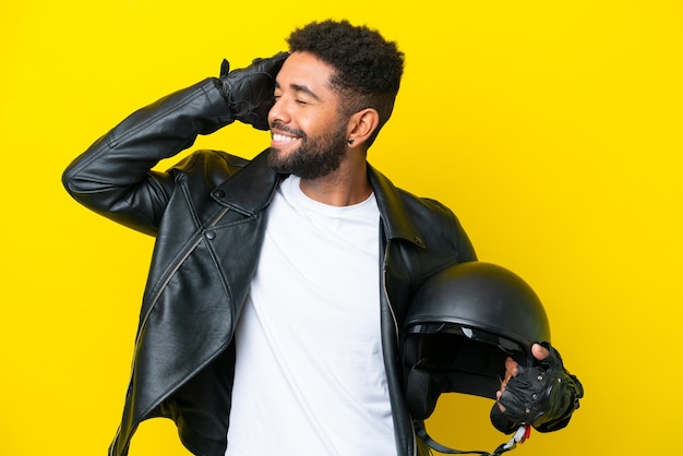 Young brazilian man with a motorcycle helmet isolated on yellow background smiling a lot