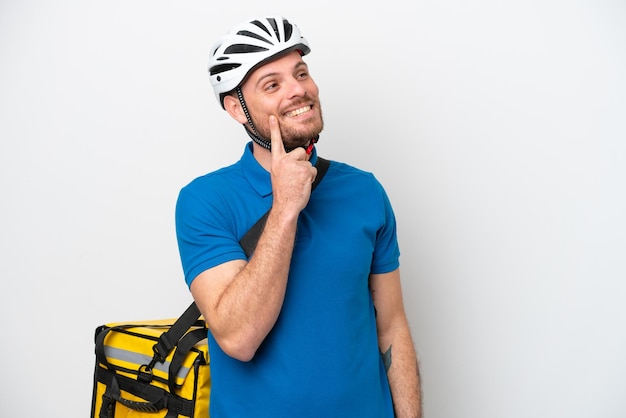 Young brazilian man with thermal backpack isolated on white background thinking an idea while looking up