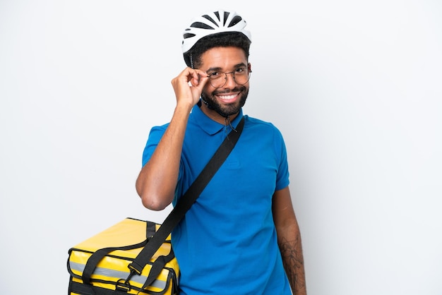 眼鏡と幸せな白い背景で隔離のサーマルバックパックを持つ若いブラジル人男性