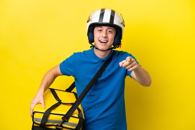 Young Brazilian man with thermal backpack isolated on yellow background surprised and pointing front