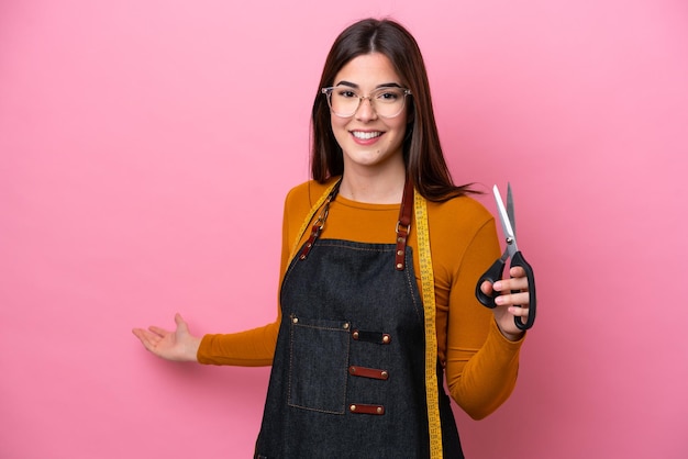 Young Brazilian seamstress woman isolated on pink background extending hands to the side for inviting to come