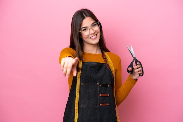 Young Brazilian seamstress woman isolated on pink background pointing front with happy expression