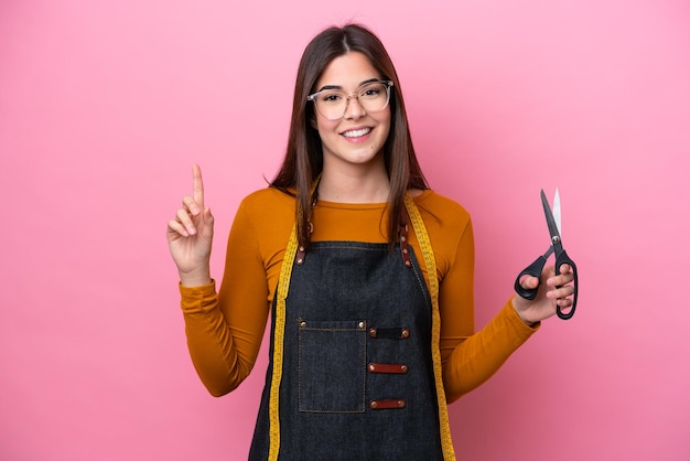 Young Brazilian seamstress woman isolated on pink background pointing up a great idea