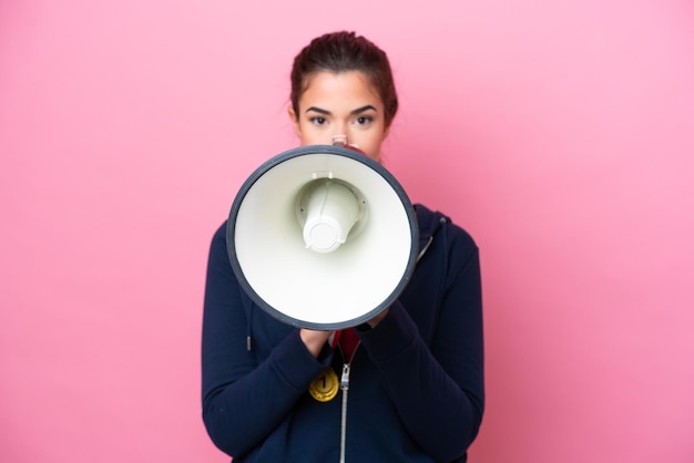 Photo young brazilian sport woman with medals isolated on pink background shouting through a megaphone