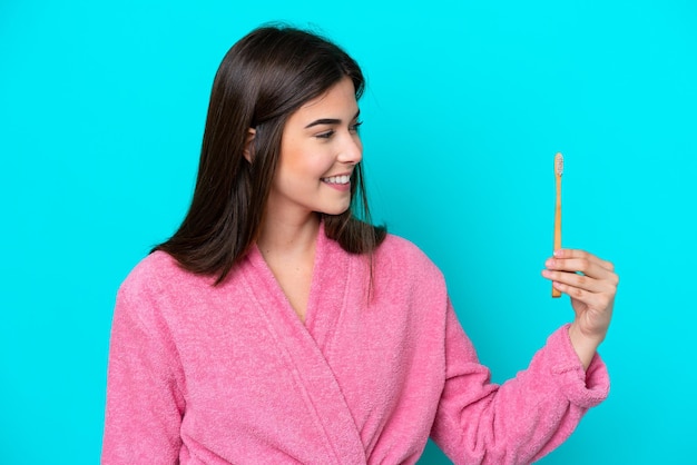 Young Brazilian woman brushing teeth isolated on blue background with happy expression