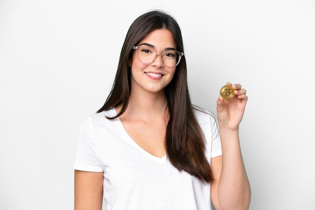 Young Brazilian woman holding a Bitcoin isolated on white background smiling a lot