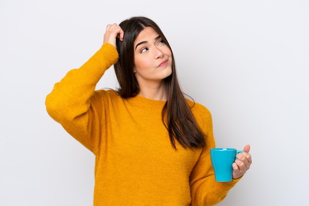 Young Brazilian woman holding cup of coffee isolated on white background having doubts and with confuse face expression