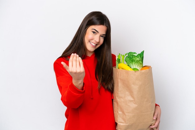 Young Brazilian woman holding a grocery shopping bag isolated on white background inviting to come with hand Happy that you came