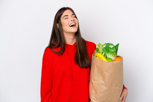 笑っている白い背景で隔離の食料品の買い物袋を保持している若いブラジル人女性