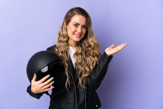 Young Brazilian woman holding a motorcycle helmet isolated on purple extending hands to the side for inviting to come