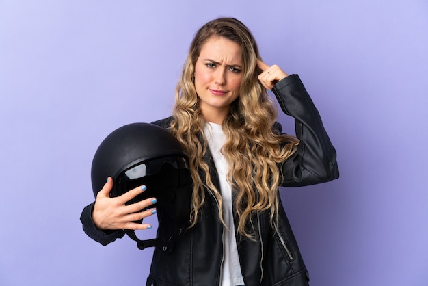 Young Brazilian woman holding a motorcycle helmet isolated on purple  having doubts and thinking