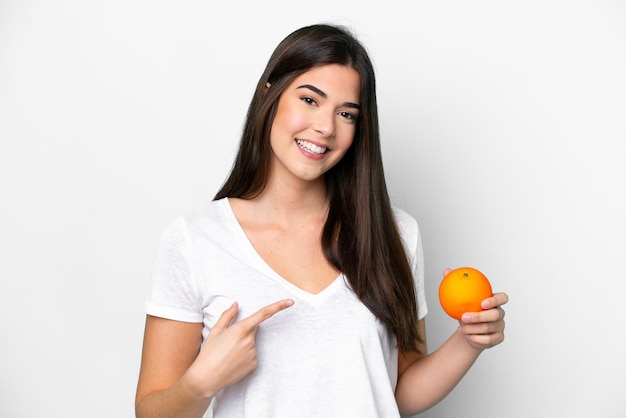 Young Brazilian woman holding an orange isolated on white background and pointing it