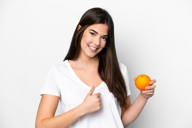 Young Brazilian woman holding an orange isolated on white background with thumbs up because something good has happened