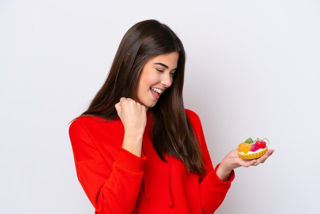 Young Brazilian woman holding a tartlet isolated on white background celebrating a victory